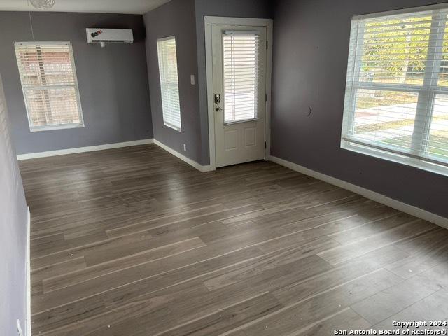 interior space with dark hardwood / wood-style flooring, a wall unit AC, and a wealth of natural light