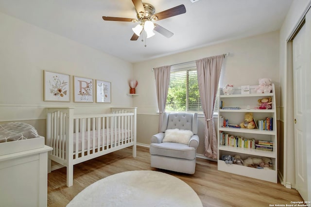 bedroom featuring a crib, light wood-type flooring, and ceiling fan