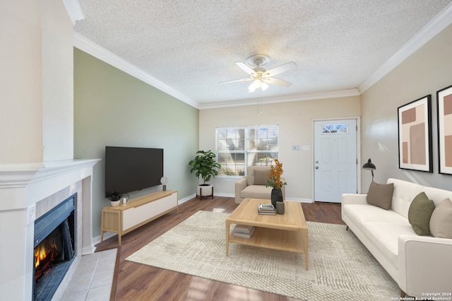 living room with a tile fireplace, wood-type flooring, a textured ceiling, and crown molding