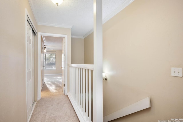 hallway with light carpet, ornamental molding, and a textured ceiling