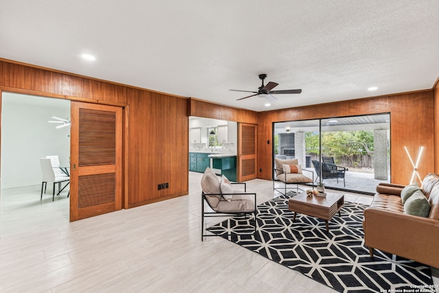 living room with ceiling fan, wooden walls, and a textured ceiling