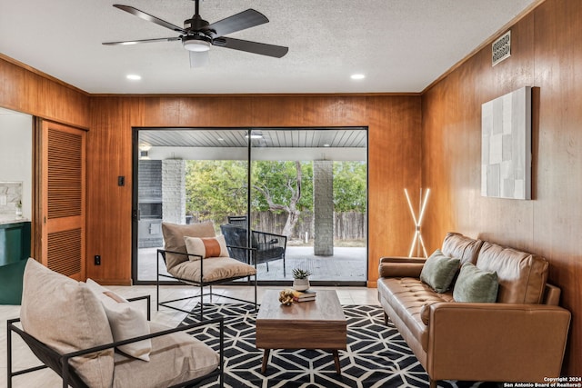 tiled living room with wood walls, ceiling fan, and a textured ceiling