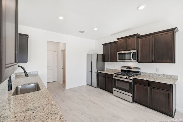 kitchen featuring light stone counters, sink, stainless steel appliances, and dark brown cabinets