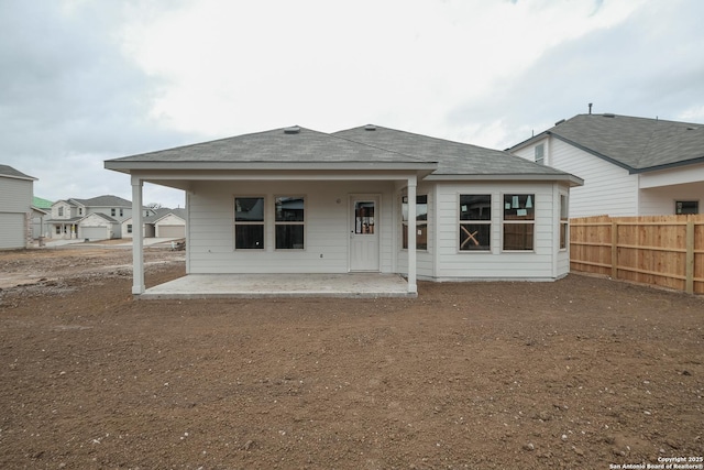 rear view of house with a patio, fence, and a shingled roof