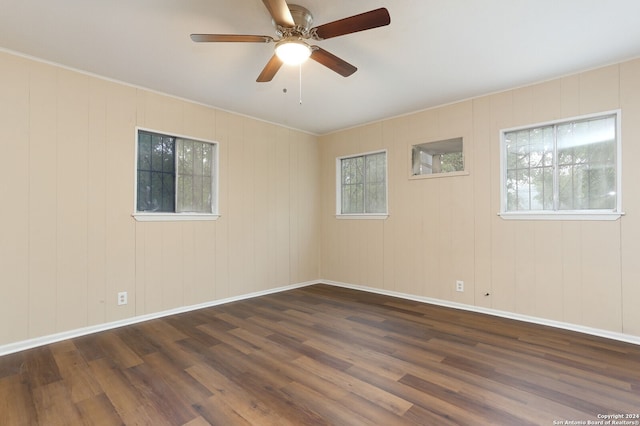 empty room featuring ceiling fan, wood walls, and dark hardwood / wood-style floors