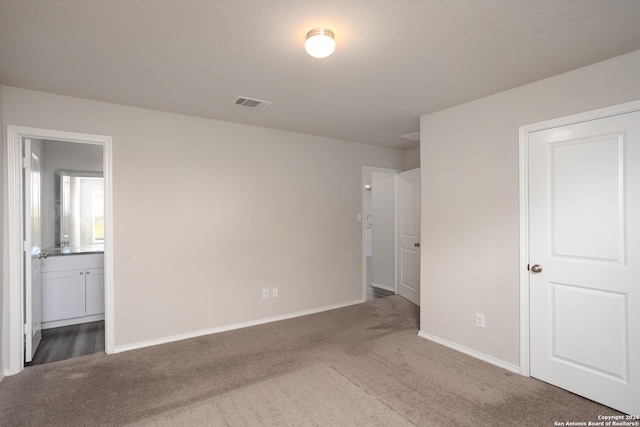 unfurnished bedroom featuring dark colored carpet, a textured ceiling, and connected bathroom