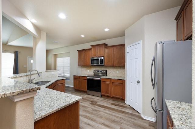 kitchen with light stone countertops, sink, stainless steel appliances, light hardwood / wood-style floors, and a kitchen island