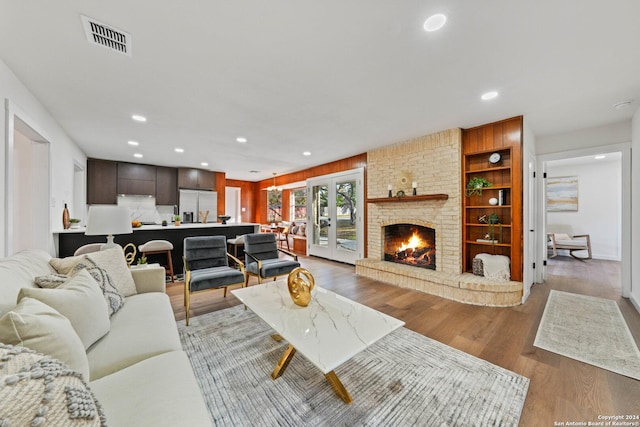 living room with wood-type flooring, built in features, a fireplace, and french doors