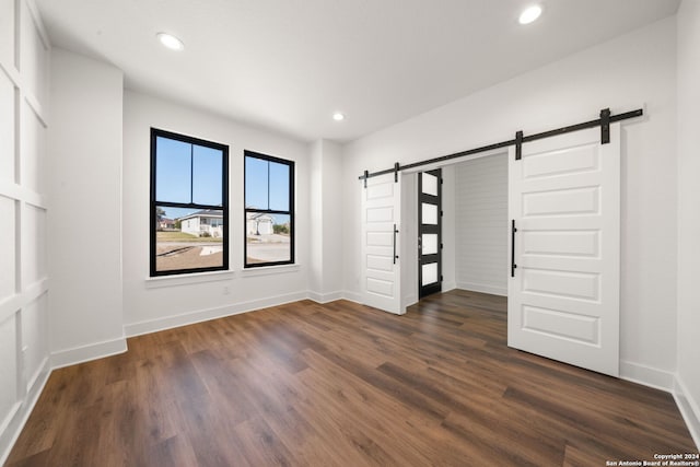 unfurnished bedroom featuring a barn door and dark wood-type flooring