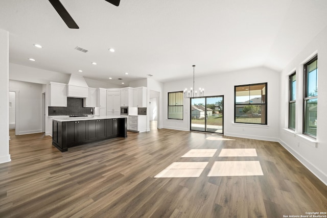 kitchen with white cabinetry, an island with sink, pendant lighting, lofted ceiling, and decorative backsplash