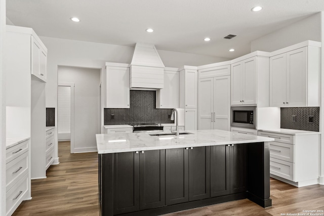 kitchen with dark hardwood / wood-style flooring, built in microwave, sink, white cabinets, and an island with sink