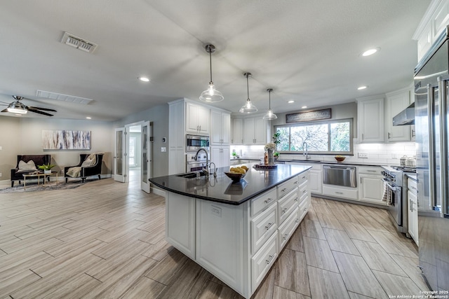 kitchen featuring white cabinetry, sink, stainless steel appliances, hanging light fixtures, and a kitchen island with sink