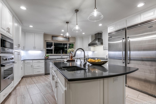 kitchen featuring white cabinetry, built in appliances, a kitchen island with sink, and wall chimney range hood