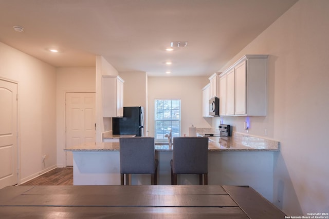 kitchen featuring light stone counters, white cabinetry, black appliances, and kitchen peninsula