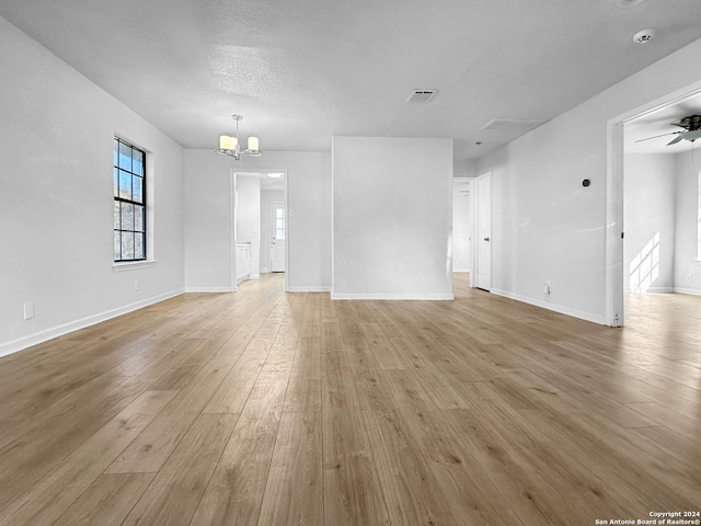 unfurnished living room with ceiling fan with notable chandelier, a textured ceiling, and light hardwood / wood-style flooring