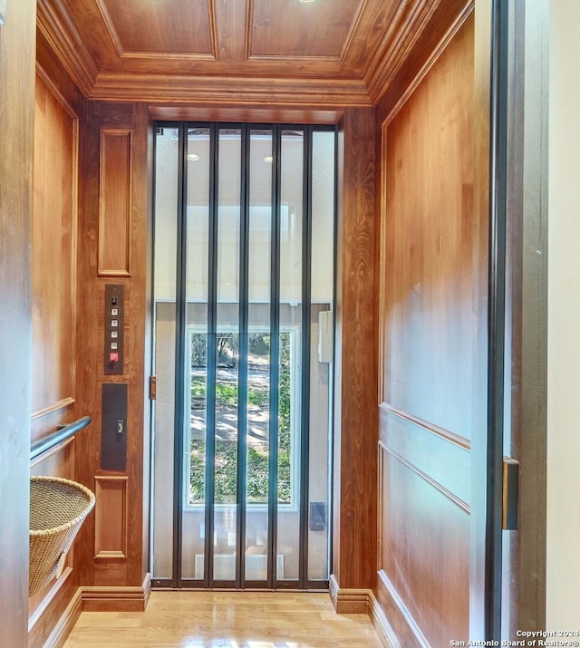 entryway with elevator, wooden ceiling, crown molding, and wooden walls