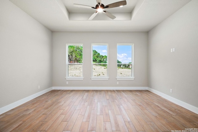 empty room featuring a tray ceiling, a wealth of natural light, ceiling fan, and light wood-type flooring