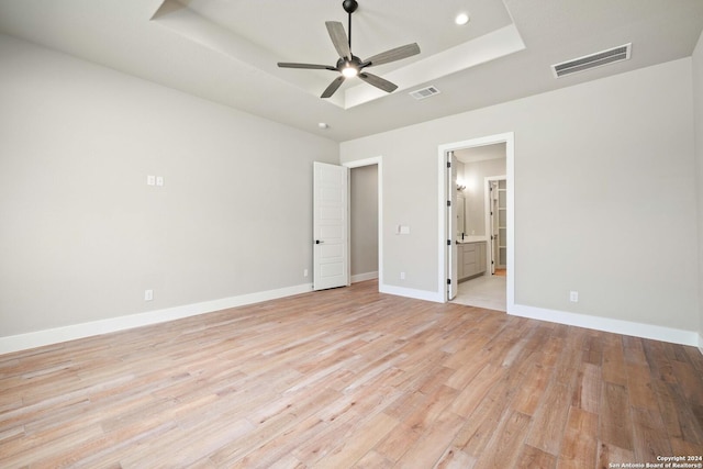 unfurnished bedroom featuring ensuite bathroom, ceiling fan, a raised ceiling, and light wood-type flooring