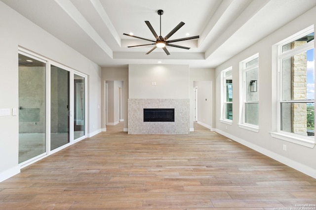 unfurnished living room with a tile fireplace, a tray ceiling, light hardwood / wood-style flooring, and ceiling fan