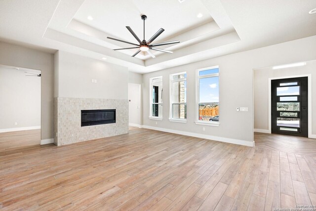 unfurnished living room featuring a tile fireplace, light hardwood / wood-style flooring, and a raised ceiling