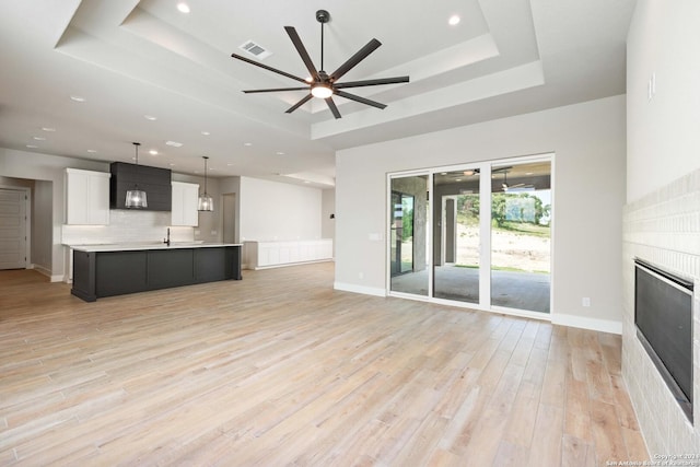 unfurnished living room featuring light wood-type flooring, a tray ceiling, ceiling fan, and sink