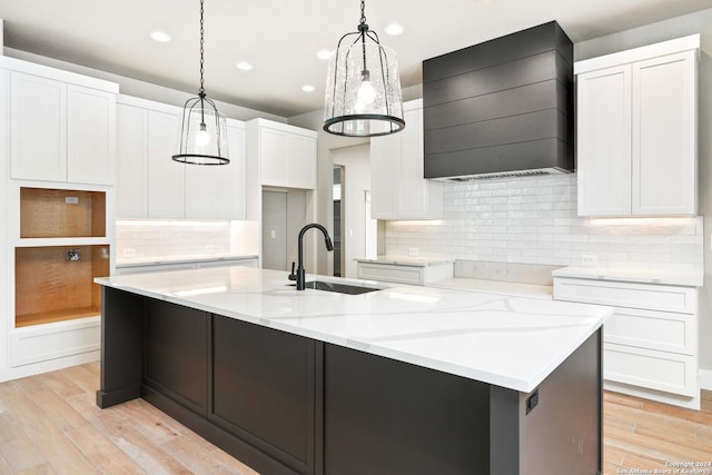 kitchen with pendant lighting, custom exhaust hood, a kitchen island with sink, sink, and white cabinetry