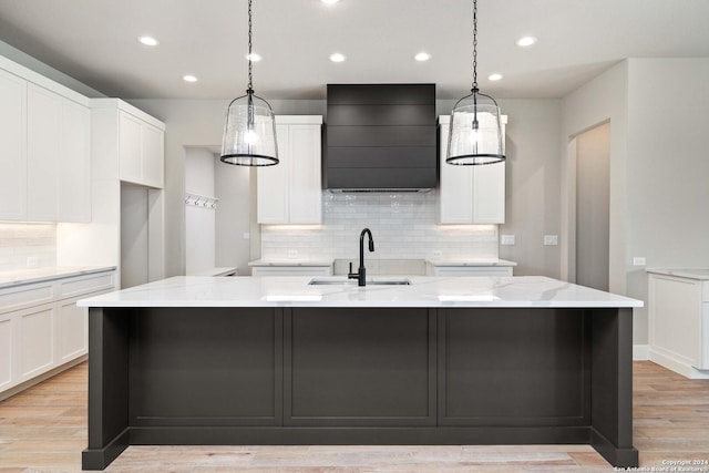 kitchen featuring light stone counters, ventilation hood, sink, white cabinetry, and a large island