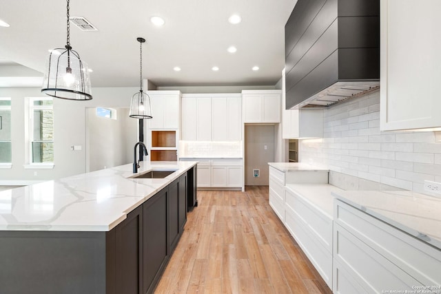 kitchen featuring premium range hood, sink, a large island with sink, decorative light fixtures, and white cabinets