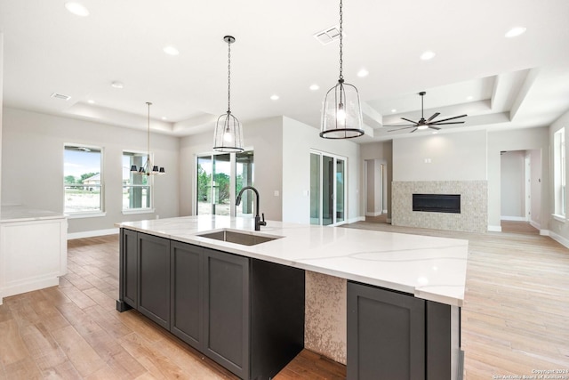 kitchen with sink, decorative light fixtures, a raised ceiling, and light stone counters