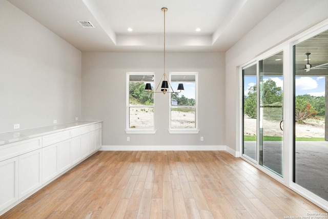 unfurnished dining area featuring ceiling fan, light hardwood / wood-style floors, and a tray ceiling