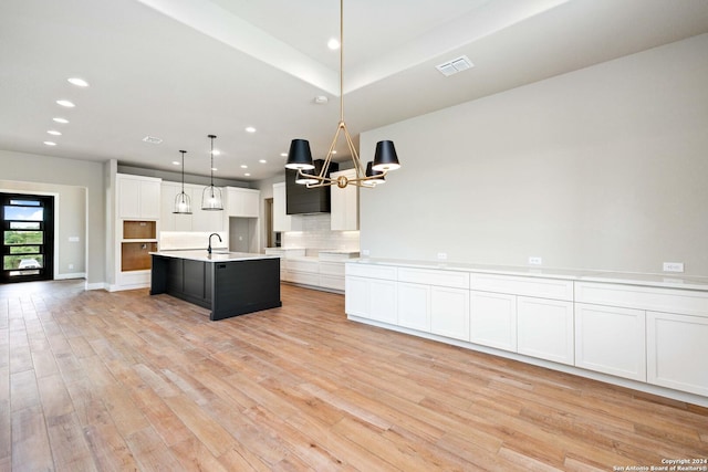 kitchen featuring sink, an island with sink, decorative light fixtures, light hardwood / wood-style floors, and white cabinetry