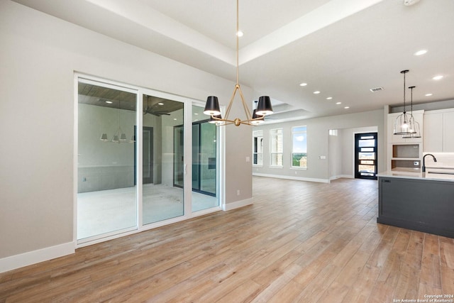 unfurnished living room with ceiling fan with notable chandelier, sink, light hardwood / wood-style flooring, and a tray ceiling