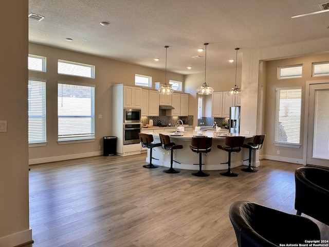 kitchen with appliances with stainless steel finishes, light wood-type flooring, a kitchen breakfast bar, hanging light fixtures, and a large island
