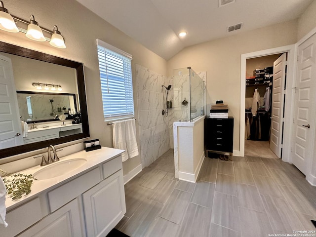 bathroom with a tile shower, vanity, and lofted ceiling
