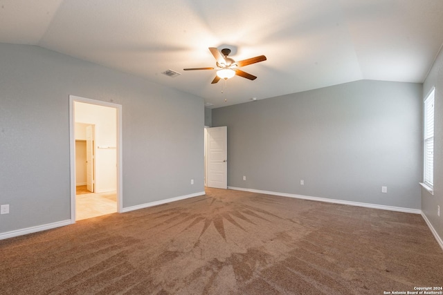 unfurnished bedroom featuring a walk in closet, light colored carpet, vaulted ceiling, and ceiling fan