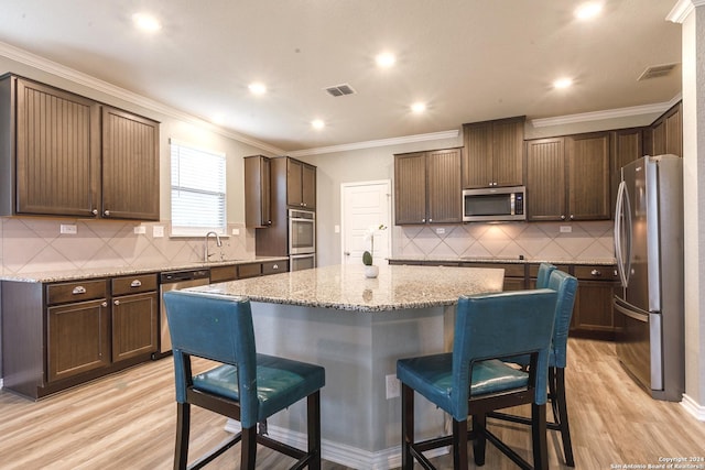 kitchen featuring a kitchen island, light stone countertops, light wood-type flooring, and stainless steel appliances