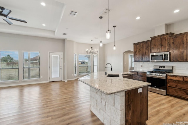 kitchen featuring tasteful backsplash, light stone counters, stainless steel appliances, a spacious island, and sink