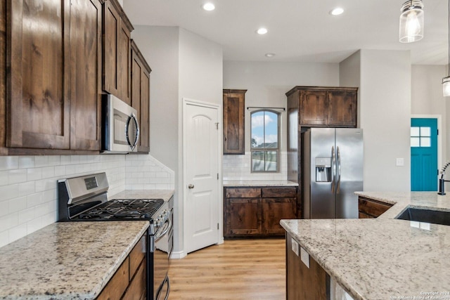 kitchen with backsplash, light stone counters, hanging light fixtures, and appliances with stainless steel finishes