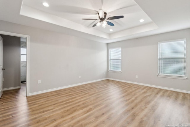 empty room with light hardwood / wood-style flooring, a raised ceiling, and ceiling fan