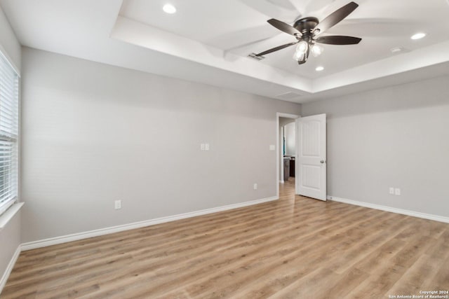 spare room with a tray ceiling, ceiling fan, and light hardwood / wood-style floors