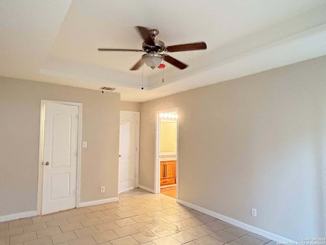 empty room with a tray ceiling, ceiling fan, and light tile patterned floors