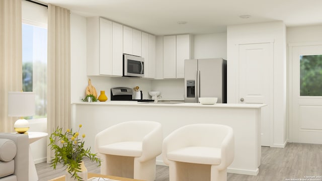 kitchen with a kitchen bar, kitchen peninsula, light wood-type flooring, stainless steel appliances, and white cabinetry