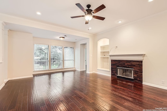 unfurnished living room featuring built in shelves, ceiling fan, dark wood-type flooring, crown molding, and a fireplace