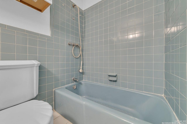 bathroom featuring tiled shower / bath combo, toilet, and tile walls