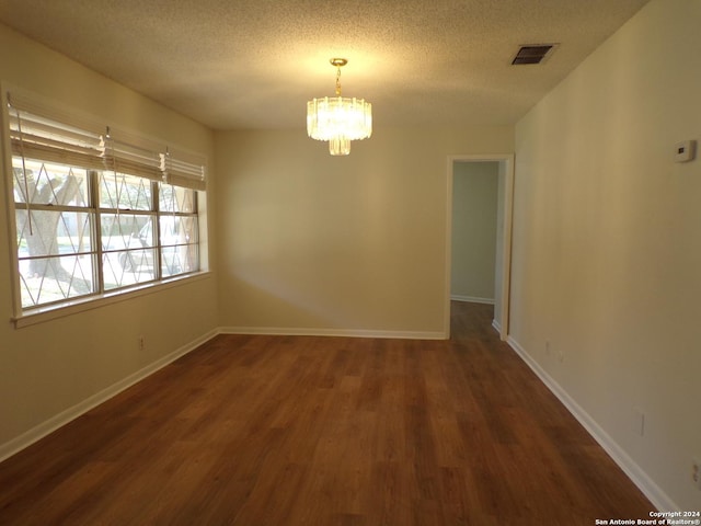 spare room featuring a textured ceiling, dark hardwood / wood-style floors, and an inviting chandelier