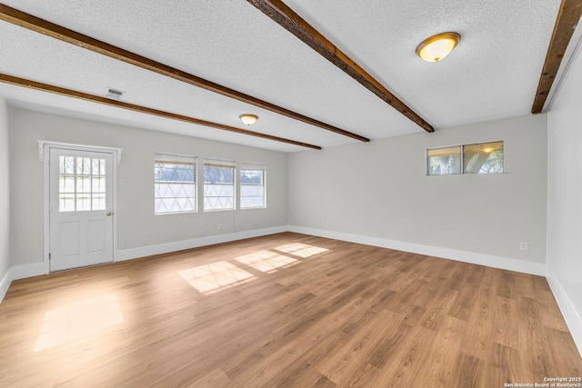 interior space featuring beamed ceiling, light hardwood / wood-style floors, and a textured ceiling