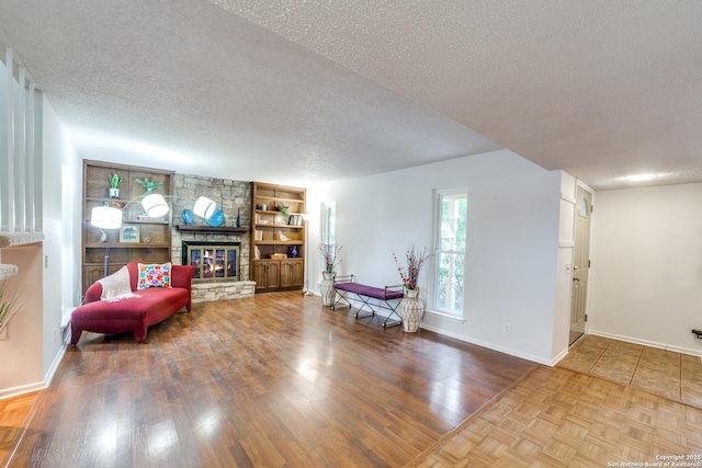 sitting room with built in shelves, wood-type flooring, a stone fireplace, and a textured ceiling