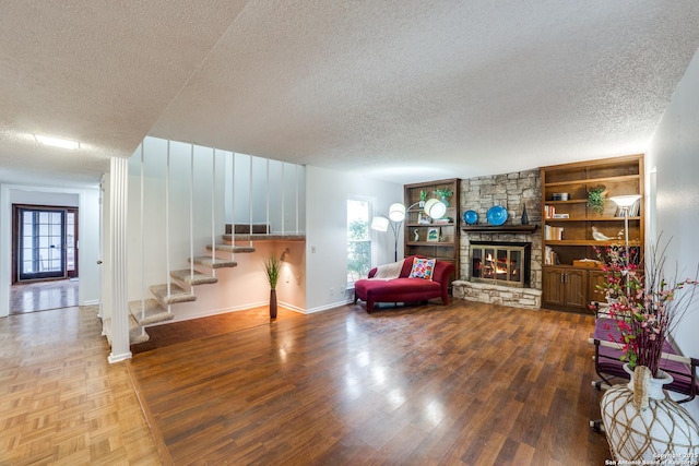 living room featuring wood-type flooring, a textured ceiling, built in features, and a stone fireplace