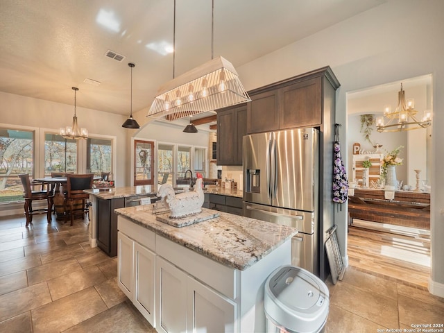 kitchen with pendant lighting, stainless steel fridge with ice dispenser, a kitchen island, light stone counters, and dark brown cabinetry