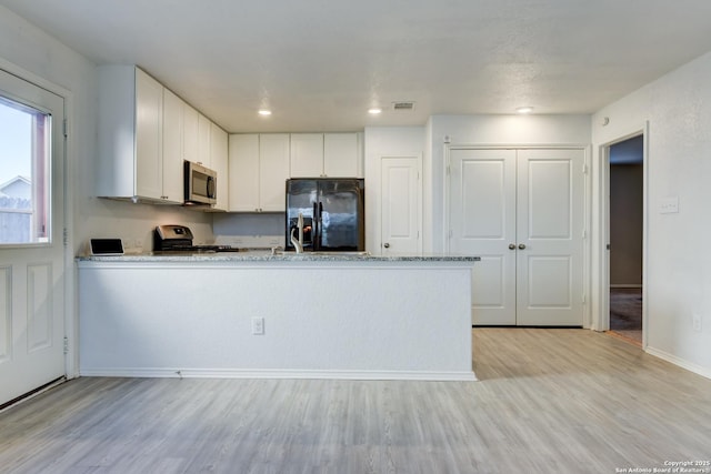 kitchen featuring appliances with stainless steel finishes, white cabinetry, light hardwood / wood-style floors, kitchen peninsula, and light stone counters